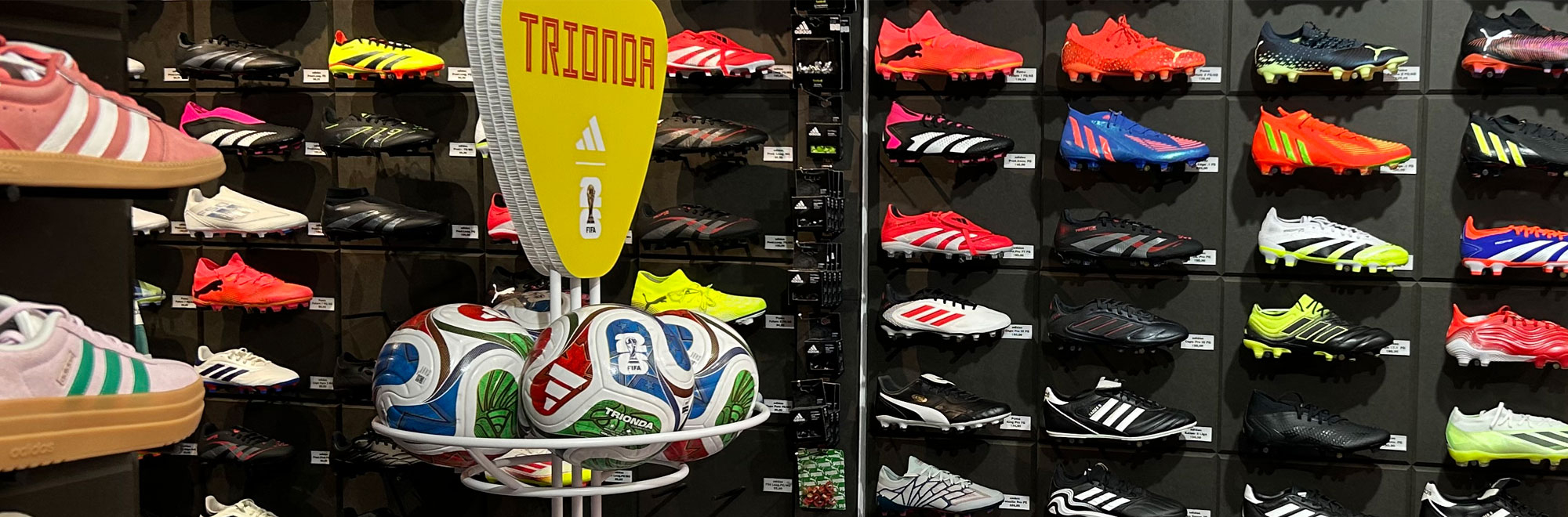 Auswahl an bunten Fußballschuhen und Adidas-Trionda-Fußbällen im Ladengeschäft domsport in Erfurt, Paulstraße 16. Große Marken wie Adidas und Puma für Vereins- und Teamsportbedarf. Fußballschuhe, Trainingsausrüstung und Sportbekleidung vor Ort in Erfurt kaufen.